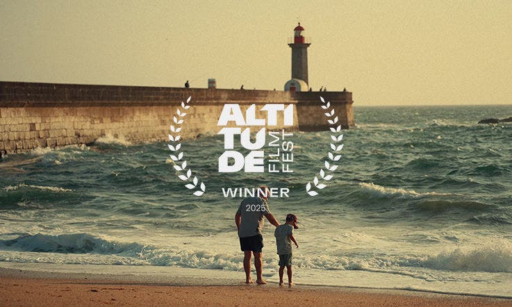 Homem caminha de mãos dadas com uma criança à beira-mar, junto a um paredão de pedra e farolim numa praia; destaque para o logótipo Altitude Film Fest, com a indicação de prémio Winner 2025, sobreposto ao centro da imagem. Homem caminha de mãos dadas com uma criança à beira-mar, junto a um paredão de pedra e farolim numa praia; destaque para o logótipo Altitude Film Fest, com a indicação de prémio Winner 2025, sobreposto ao centro da imagem.