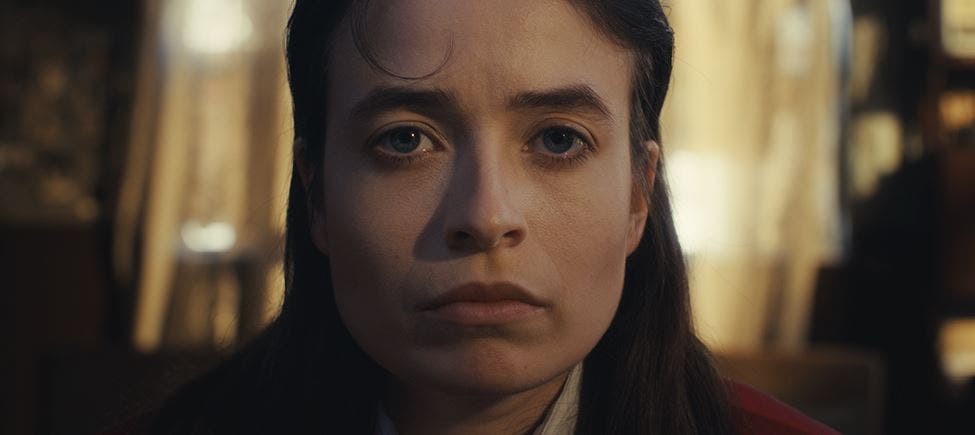 Mulher jovem de expressão séria e olhar fixo, com cabelo castanho escuro, fotografada em primeiro plano e fundo desfocado iluminado por luz dourada. Mulher jovem de expressão séria e olhar fixo, com cabelo castanho escuro, fotografada em primeiro plano e fundo desfocado iluminado por luz dourada.