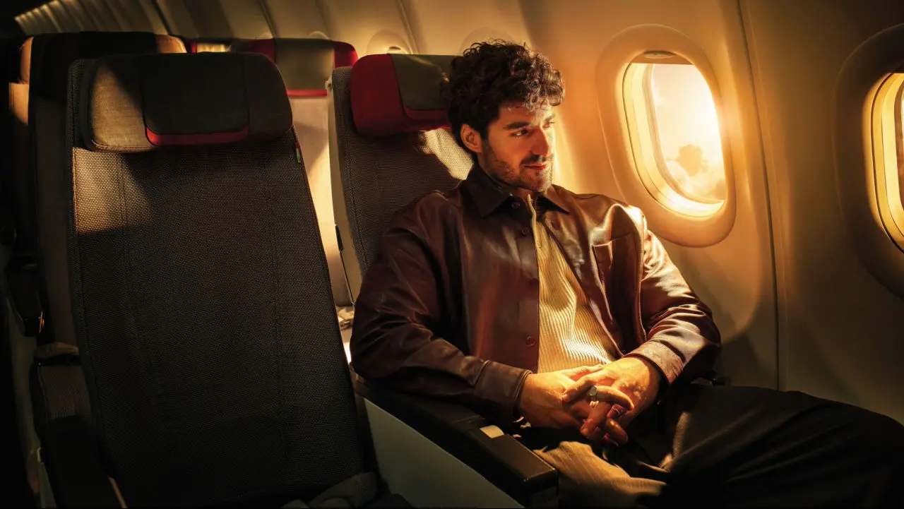 Homme assis près du hublot d’un avion, éclairé par une lumière dorée, avec une expression calme et détendue.