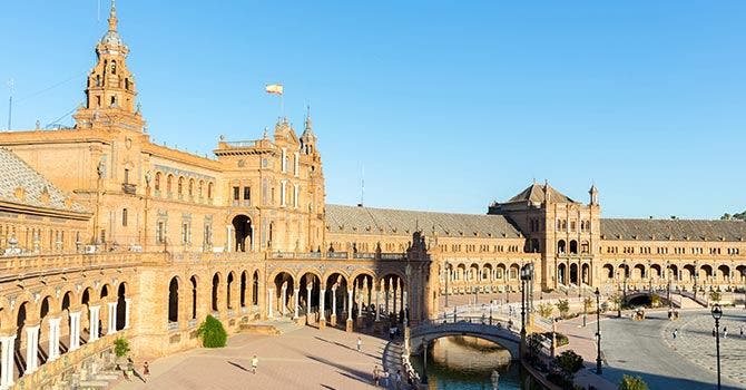 La Plaza de España à Séville, avec des bâtiments historiques de style Renaissance, des arcades et un canal sous un ciel bleu.