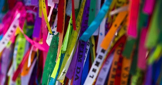 Close-up de fitas coloridas do Senhor do Bonfim com inscrições em português, penduradas lado a lado, formando um fundo vibrante.