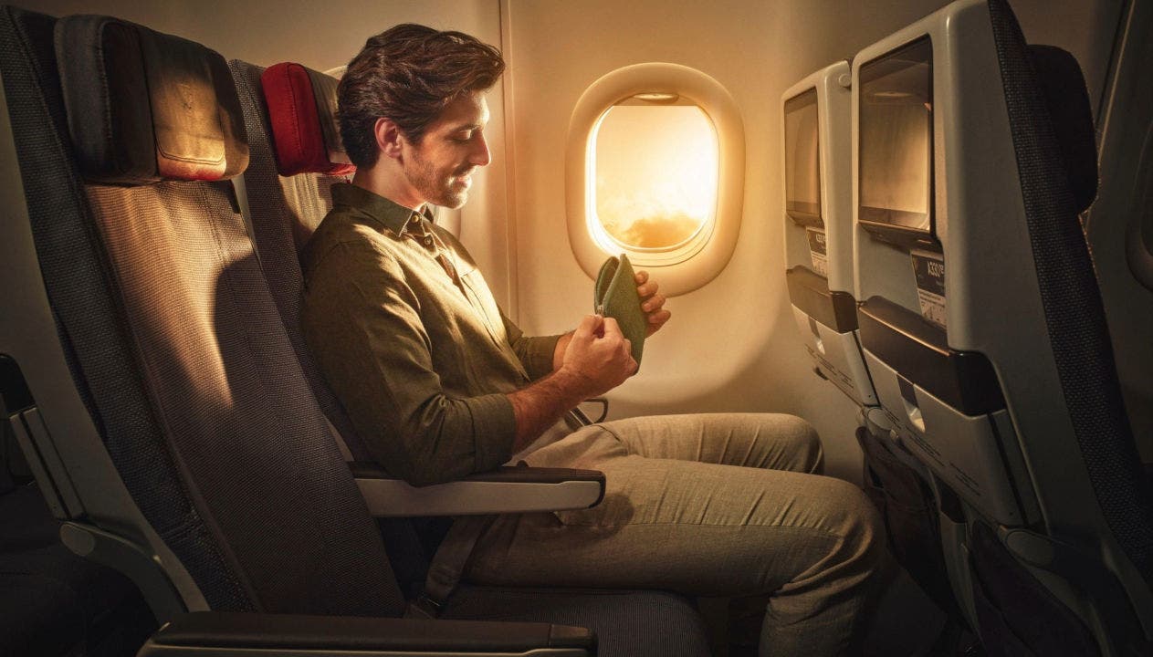 Un homme assis près du hublot d’un avion sourit en rangeant un petit objet personnel, éclairé par la lumière du soleil, avec le siège à côté de lui vide. Un homme assis près du hublot d’un avion sourit en rangeant un petit objet personnel, éclairé par la lumière du soleil, avec le siège à côté de lui vide.