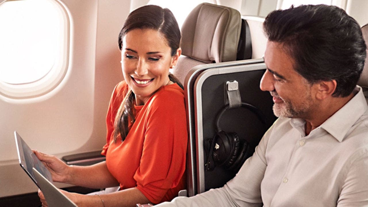 Fotografia de um homem e de uma mulher sorridentes sentados abordo de um avião TAP em classe Executiva. A mulher, morena, usa o cabelo apanhado, encontra-se vestida com uma blusa vermelha e segura um tablet para o qual está a olhar. O Homem, moreno, com barba branca, veste uma camisa branca e está a olhar para o tablet que a mulher segura. Fotografia de um homem e de uma mulher sorridentes sentados abordo de um avião TAP em classe Executiva. A mulher, morena, usa o cabelo apanhado, encontra-se vestida com uma blusa vermelha e segura um tablet para o qual está a olhar. O Homem, moreno, com barba branca, veste uma camisa branca e está a olhar para o tablet que a mulher segura.